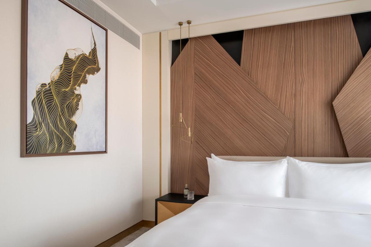 Steigenberger Hotel Doha Exterior photo The photo shows a modern hotel room with a clean and stylish design. The focal point is a large bed with white linens, set against a wall that features contemporary wooden paneling with geometric shapes. On the left side, there is a piece of artwork 