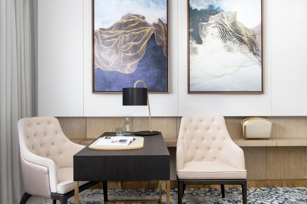 Steigenberger Hotel Doha Exterior photo The photo shows a stylish and modern office space. There are two elegant framed artworks on the walls, characterized by abstract designs with soft colors and fluid lines. In the center, there’s a black desk with a white notepad and a pen. A sleek, bl