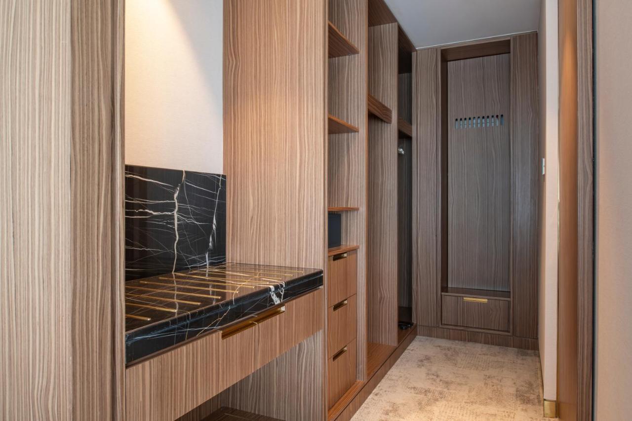 Steigenberger Hotel Doha Exterior photo The photo shows a well-designed interior space, likely a closet or dressing area. It features wooden cabinetry with a modern finish, including several open shelves for storage. There's a section with a dark marble countertop, which adds an elegant to