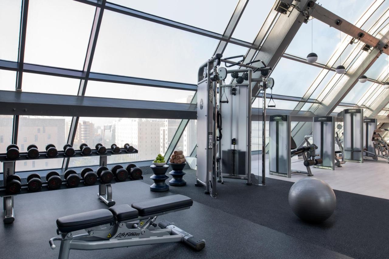 Steigenberger Hotel Doha Exterior photo The photo shows a modern gym with large glass windows allowing natural light to fill the space. The gym is equipped with various fitness equipment, including a cable machine, a weight bench, and free weights arranged neatly on a rack. A stability bal