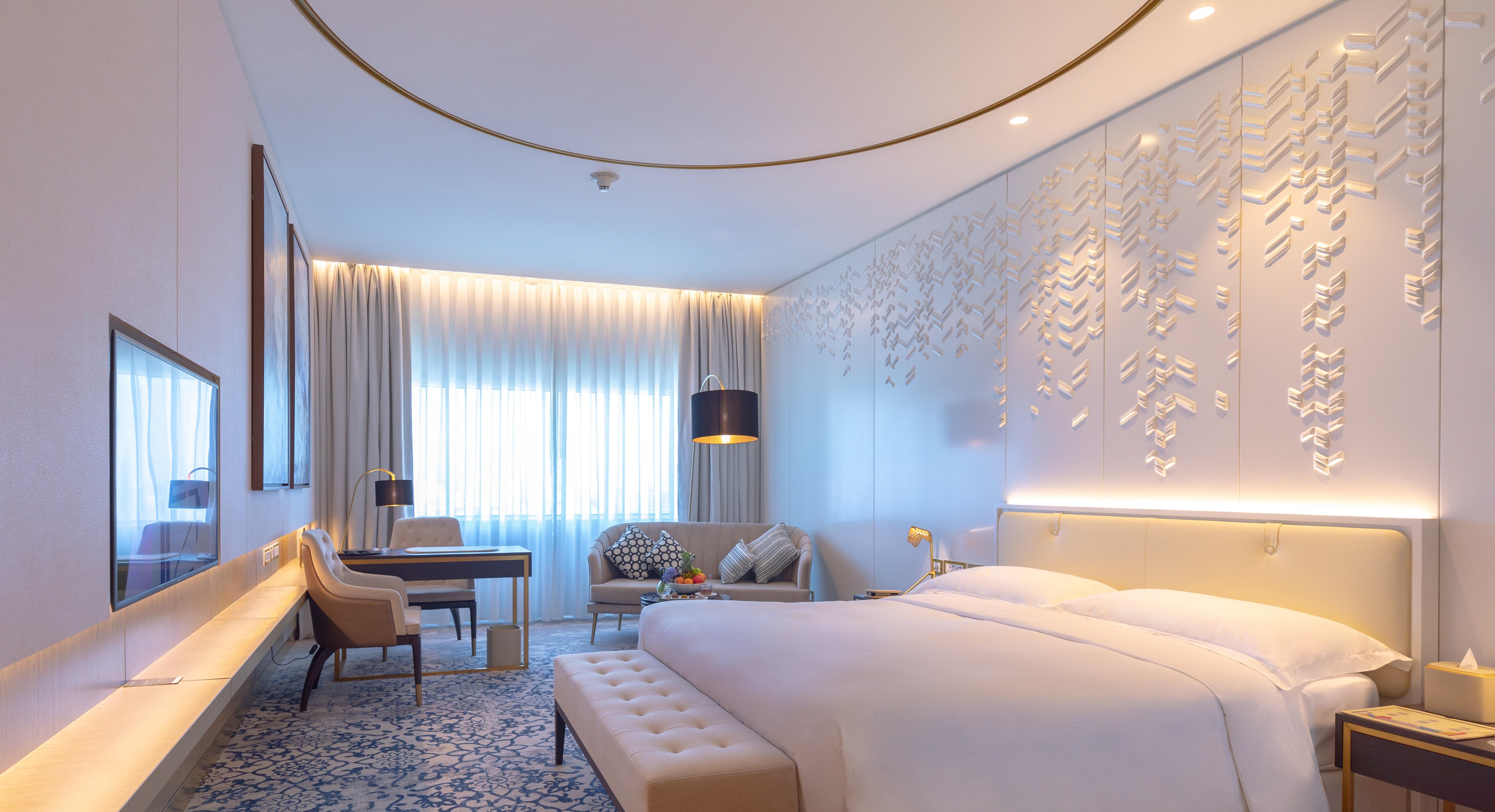 Steigenberger Hotel Doha Exterior photo The photo shows a modern and elegantly designed hotel room. It features a large bed with a light-colored headboard and plush bedding. The room includes a seating area with a sofa and armchair, complemented by decorative cushions. There is also a desk