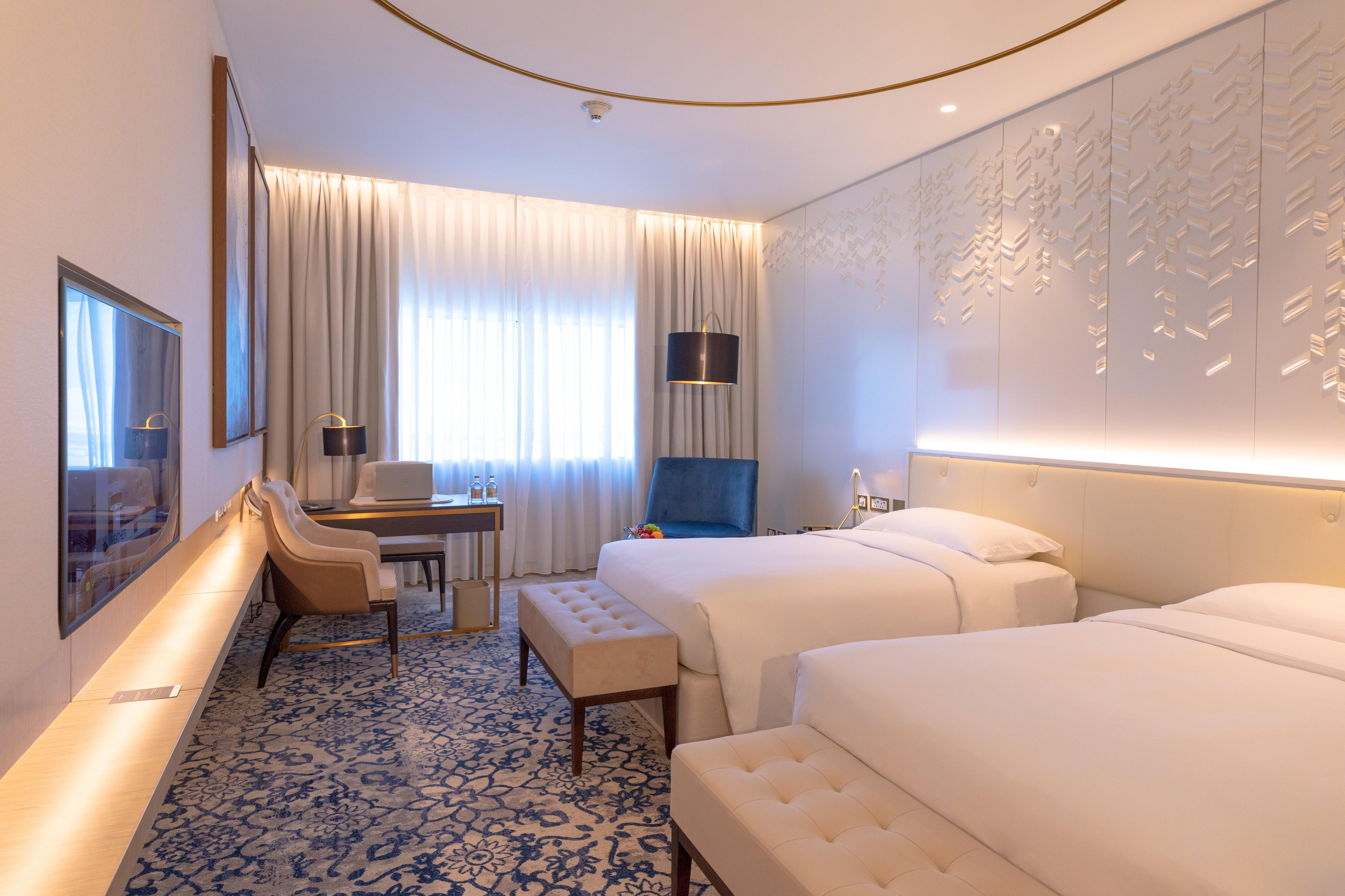Steigenberger Hotel Doha Exterior photo The photo shows a modern hotel room with two single beds placed beside each other. The room features a contemporary design with light-colored walls and stylish decor. There is a large window dressed with sheer curtains, allowing natural light to fill