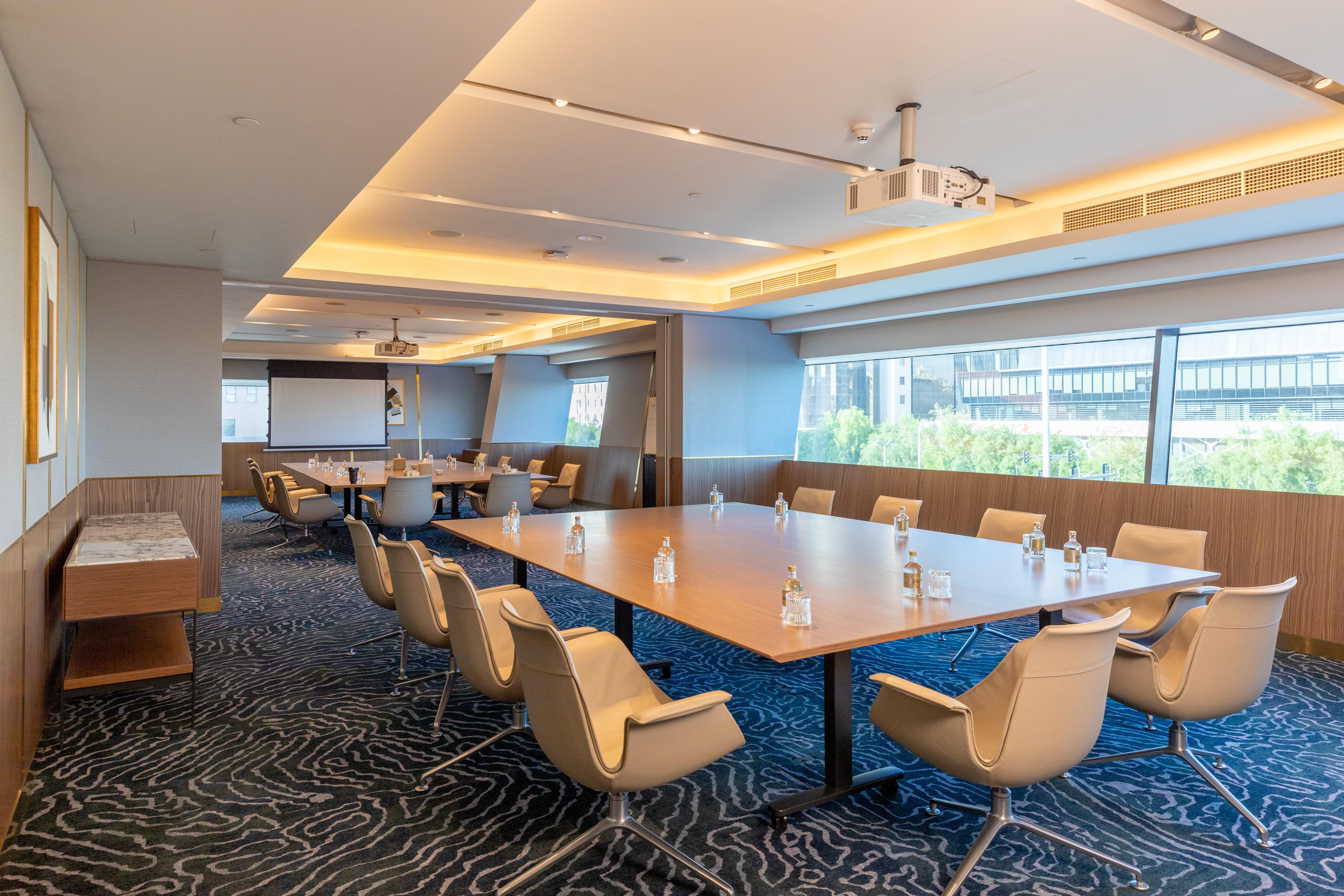Steigenberger Hotel Doha Exterior photo The photo shows a modern conference room. It features large windows that let in natural light, illuminating the space. In the center, there is a large rectangular table surrounded by several ergonomic chairs. The table has glass water bottles on it, 