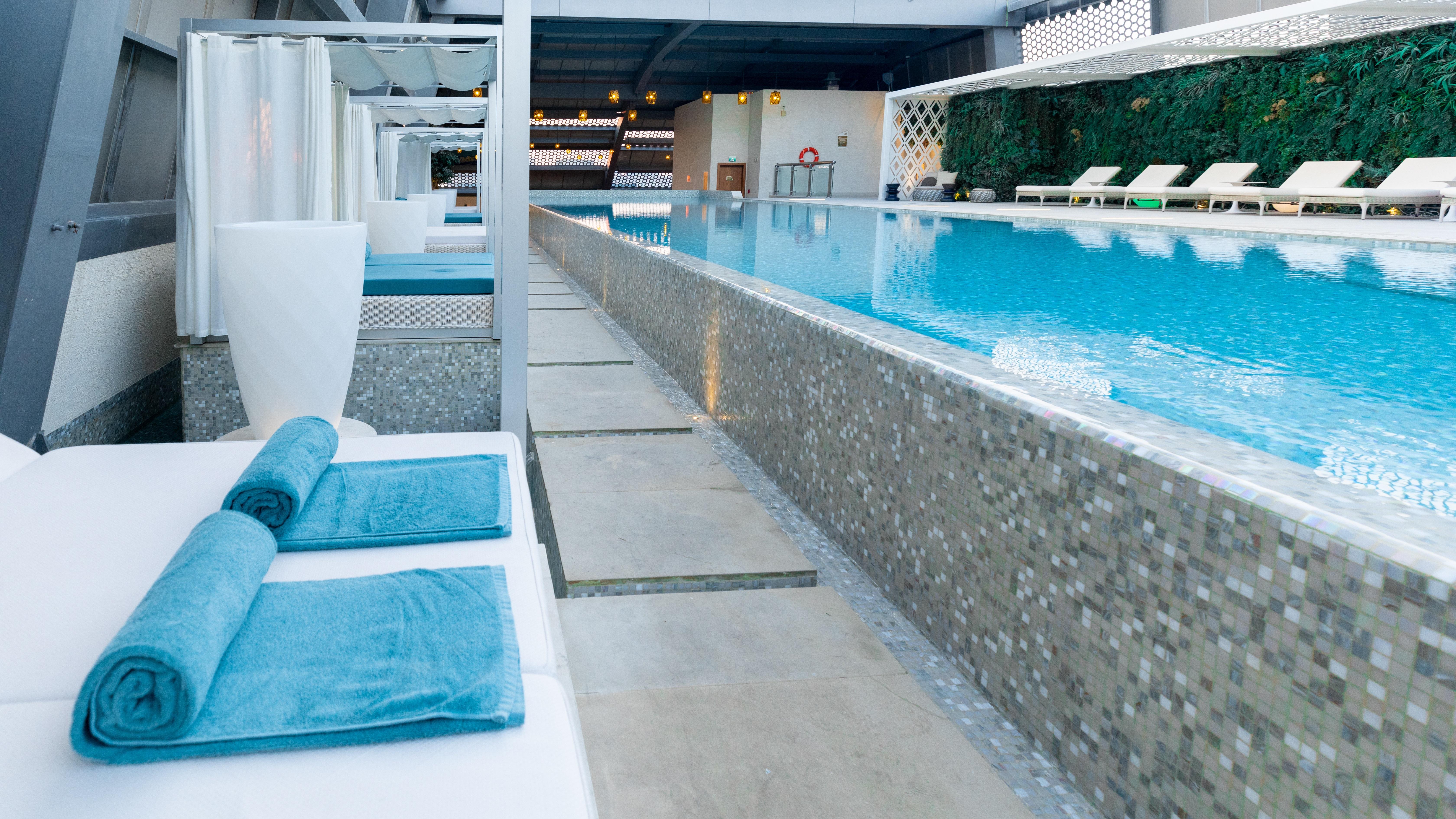 Steigenberger Hotel Doha Exterior photo The photo shows a serene swimming pool area featuring a long, rectangular pool with clear blue water. Surrounding the pool are minimalist white lounge chairs and cabanas, creating a relaxing atmosphere. The pool is bordered by a stone or tile pathway