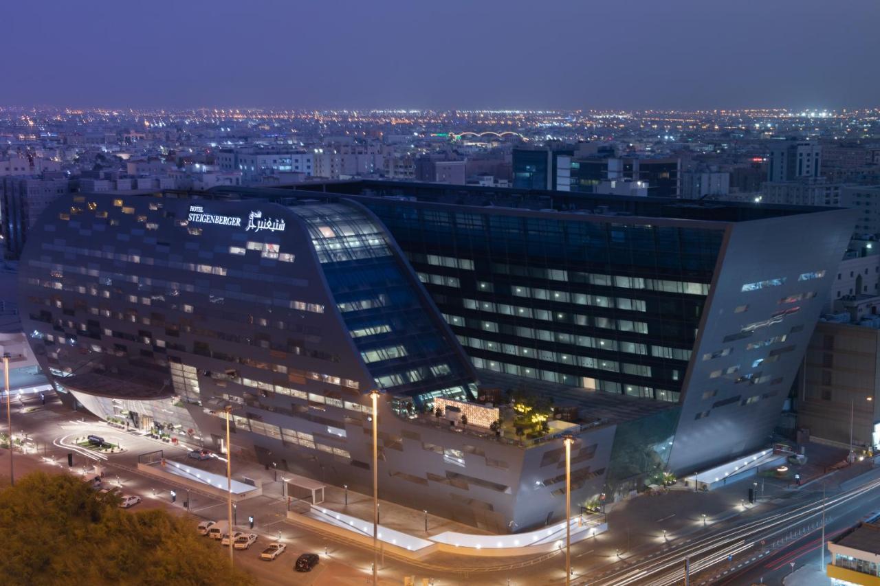 Steigenberger Hotel Doha Exterior photo The image shows a modern architectural building, likely a hotel or office structure, illuminated at night. The design features a unique angular shape with large glass windows, reflecting the surrounding city lights. The building appears to be part of