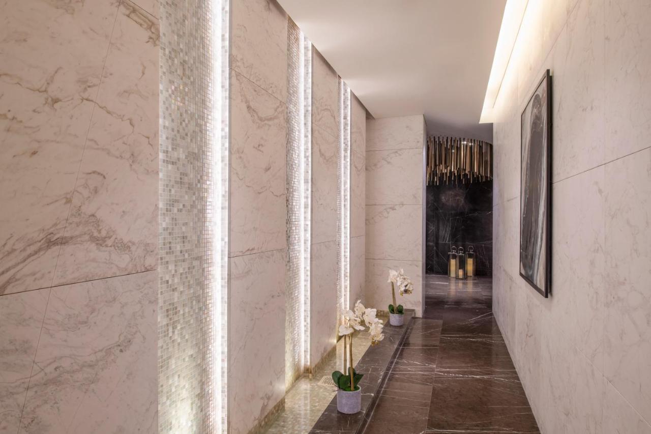 Steigenberger Hotel Doha Exterior photo The photo shows a modern hallway with stylish design elements. The walls are made of light-colored marble, and there are vertical strips of lighting integrated into the stone. The floor appears to be a darker stone, providing a contrast to the walls.