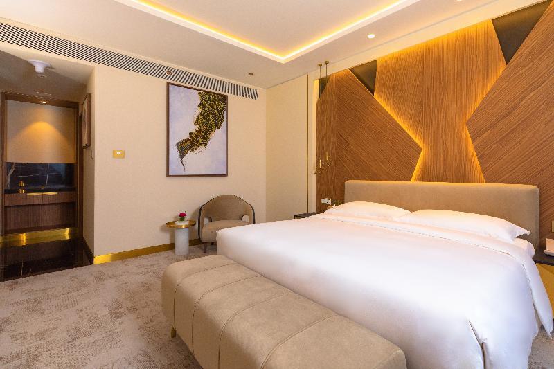 Steigenberger Hotel Doha Exterior photo The photo shows a modern hotel room featuring a comfortable bed with a plush white duvet, flanked by elegant decorative elements. The headboard has a stylish wood grain design, accompanied by warm lighting that creates a cozy atmosphere. A small seat