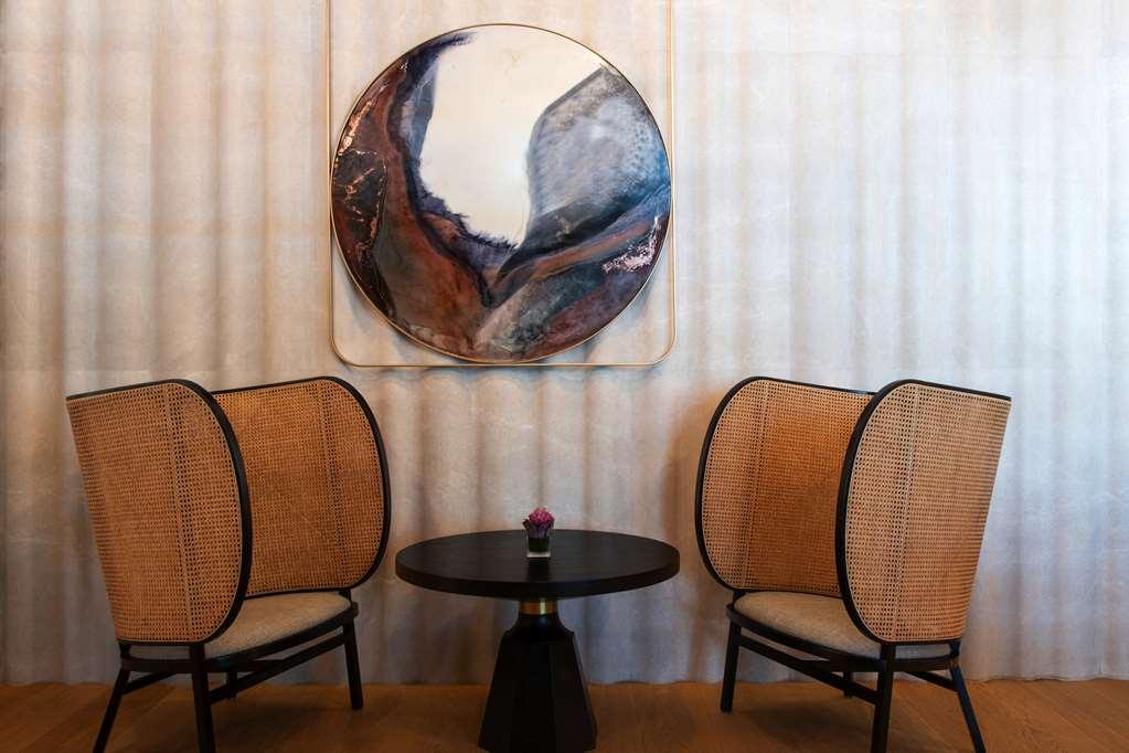 Steigenberger Hotel Doha Restaurant photo The photo showcases a stylish and modern seating area featuring two elegantly designed chairs with curved, woven backs and light-colored cushions. Between the chairs is a small round table with a black base. Above the table hangs a large circular art